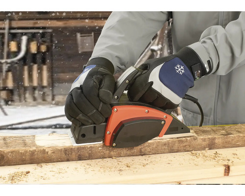 Osoba hobluje dřevěnou desku elektrickým hoblíkem venku.