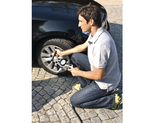 Muž hustí pneumatiku automobilu pomocí měřiče tlaku v pneumatikách.
