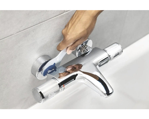Snímek ruky ovládající termostatickou směšovací baterii pro vanu.