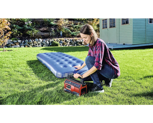 Žena nafukuje matraci elektrickou pumpou na zahradě.