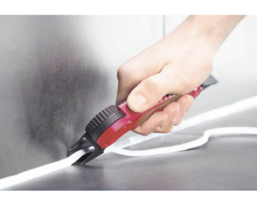 Osoba řeže bílé těsnění řezačkou spár. Nástroj má červenou rukojeť.