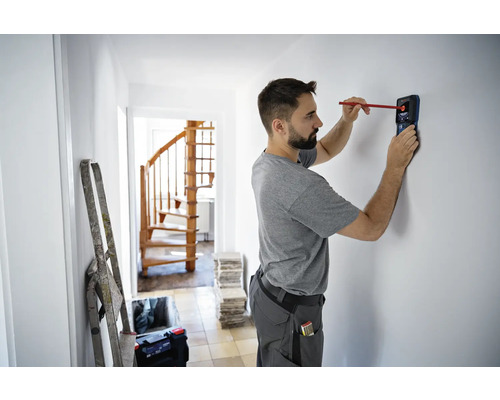 Muž používá detektor k nalezení objektů ve zdi v domě.