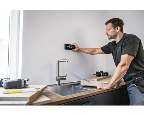 Muž používá digitální detektor na zdi v kuchyni.