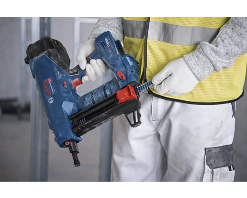 Osoba nabíjí sponky do pneumatické hřebíkovačky.