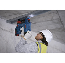 Dělník připevňuje kovovou lištu k betonovému stropu pomocí nastřelovací pistole.