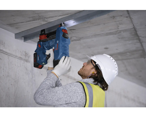 Dělník připevňuje kovovou lištu k betonovému stropu pomocí nastřelovací pistole.