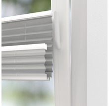 Detailní pohled na bílou skládanou žaluzii na okně