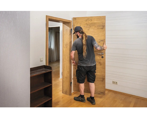 Muž instaluje interiérové dveře s dřevěným vzhledem v místnosti.