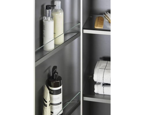 Detail koupelnové skříňky se skleněnými policemi a různými koupelnovými potřebami, jako je mýdlo, šampon, ručníky a kartáč