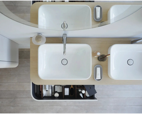 Pohled shora na koupelnu s dvojitým umyvadlem, zrcadlem a otevřenou zásuvkou s koupelnovými potřebami