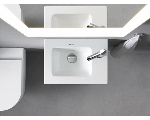 Pohled shora na koupelnu s umyvadlem, zrcadlem s osvětlením, ručníkem a toaletou.