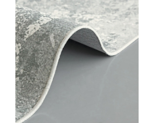 Detailní pohled na šedý koberec s abstraktním vzorem a obšitými okraji