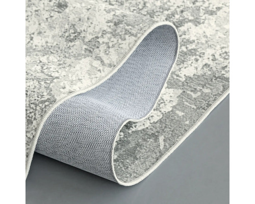 Šedý koberec s abstraktním vzorem, částečně srolovaný, aby ukázal zadní stranu