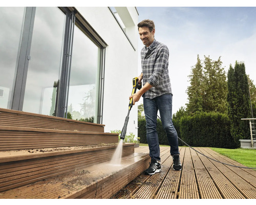 Muž čistí dřevěnou terasu vysokotlakým čističem u domu