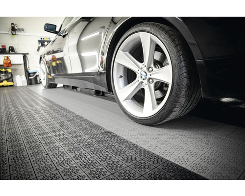 Černé auto na podlaze garáže s dlaždicovou strukturou.