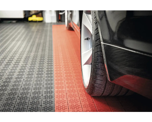 Detailní záběr černého auta na garážových dlaždicích v šedé a červené barvě.