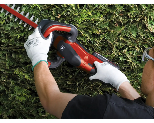 Osoba používá nůžky na živý plot a má na sobě ochranné rukavice.