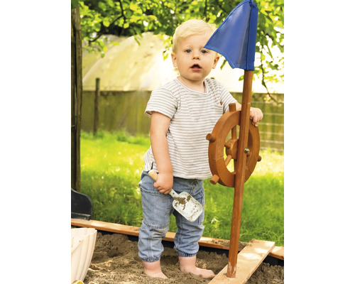 Batole si hraje s herní lodí s volantem a modrou vlajkou v pískovišti