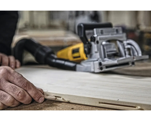 Osoba používá drážkovací frézu na dřevěné desce k vytvoření drážky.