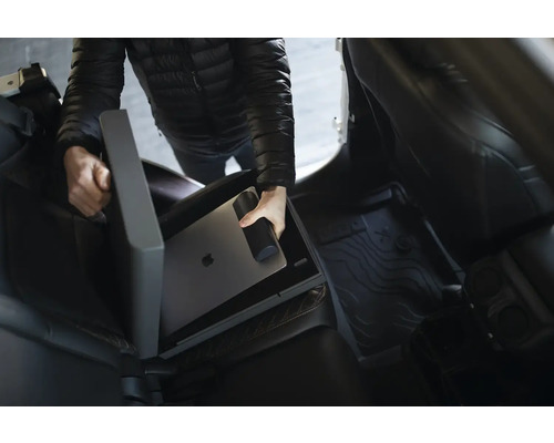 Osoba ukládá notebook a láhev na pití do úložného boxu do auta