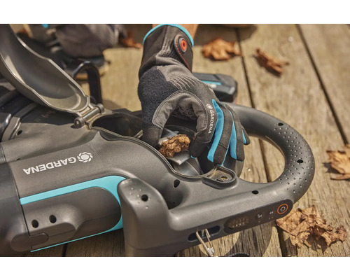 Akumulátorový vysavač listí Gardena s otevřenou klapkou a rukou v zahradní rukavici, která odstraňuje listí