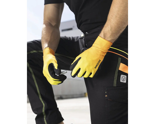 Osoba v pracovních kalhotách a pracovních rukavicích drží šroub.