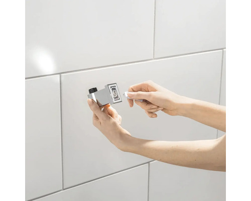 Osoba montuje magnetický dveřní zarážku na obloženou zeď