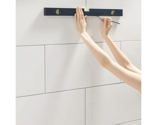 Osoba používá vodováhu a tužku k nakreslení čáry na obkládané stěně.