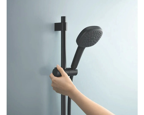 Ruka drží černou sprchovou tyč a ruční sprchu.