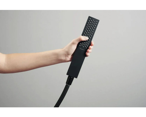 Ruka drží obdélníkovou ruční sprchu s hadicí.