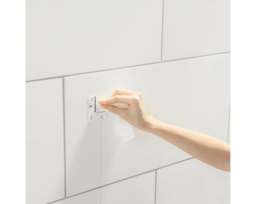 Osoba upevňuje pomocí hadříku Grohe QuickFix na obloženou stěnu