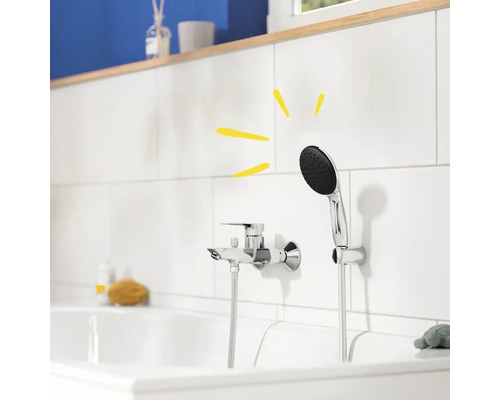 Nástěnná sprchová baterie s ruční sprchou v koupelně s bílými obklady.