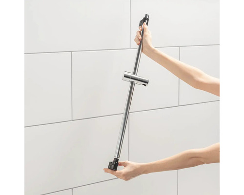 Osoba drží kovovou sprchovou tyč s nastavitelným držákem sprchové hlavice.