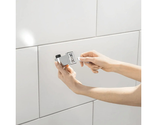 Osoba upevňuje háček na ručníky na obkládanou stěnu.