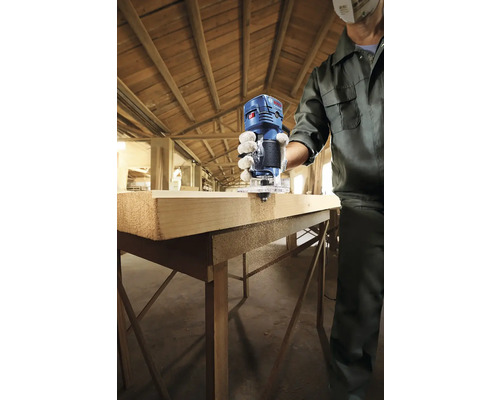 Osoba frézuje kus dřeva horní frézkou Bosch