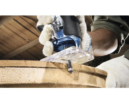 Horní frézka v akci při obrábění kusu dřeva. Operátor má na sobě pracovní rukavice.