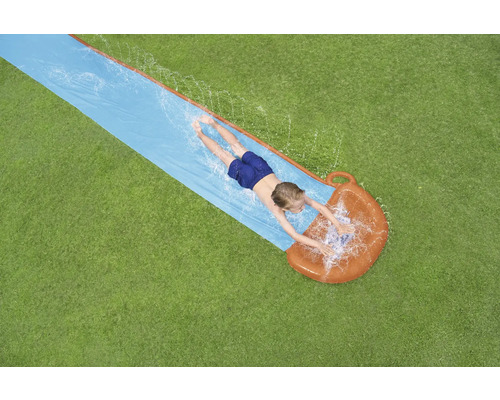 Pohled shora na dítě ležící na vodní skluzavce na zahradě