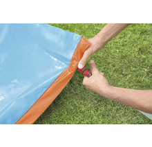 Osoba připojuje zahradní hadici k modré a oranžové vodní skluzavce na zahradě.