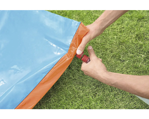 Osoba připojuje zahradní hadici k modré a oranžové vodní skluzavce na zahradě.