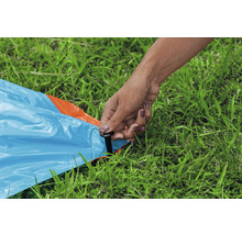 Osoba připevňuje modrou plachtu kolíkem do trávy