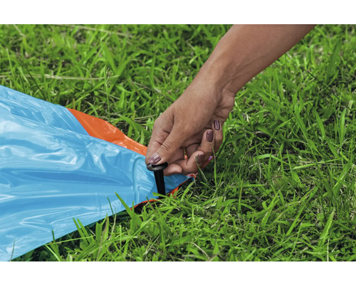Osoba připevňuje modrou plachtu kolíkem do trávy