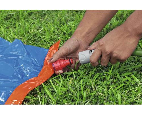 Osoba připojuje zahradní hadici k vodní skluzavce na trávníku.