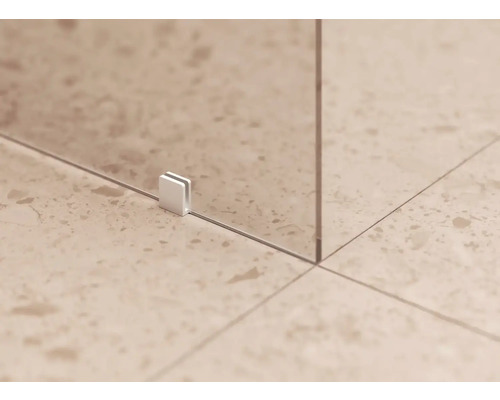 Detail skleněné sprchové stěny s upevňovací sponou na dlážděné podlaze.