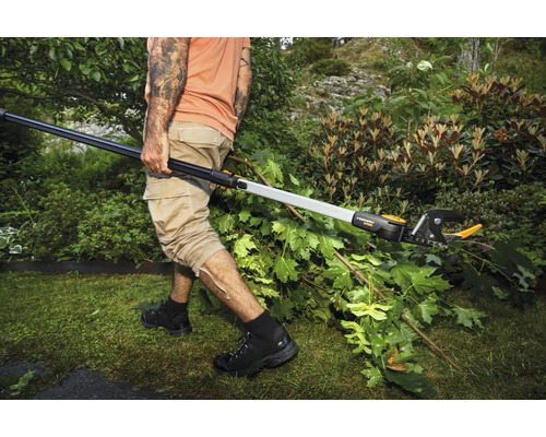 Osoba stříhá větve v zahradě pomocí teleskopických nůžek na větve.