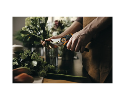 Osoba stříhá větve zahradními nůžkami Fiskars na stole.