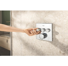 Logo Grohe. Nástěnná termostatická baterie s ručním ovládáním před obkládanou stěnou.