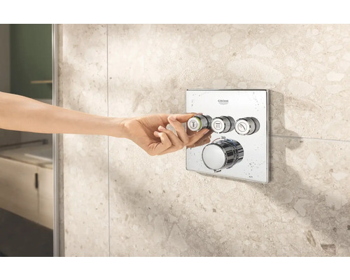 Logo Grohe. Nástěnná termostatická baterie s ručním ovládáním před obkládanou stěnou.