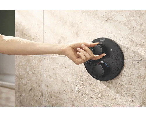 Ruka ovládá černý sprchový termostat Grohe na obkládané stěně