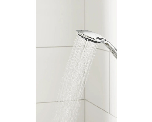 Sprchová hlavice s proudem vody před bílými dlaždicemi