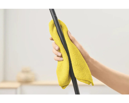 Ruka otírá černou tyč žlutým hadříkem z mikrovlákna